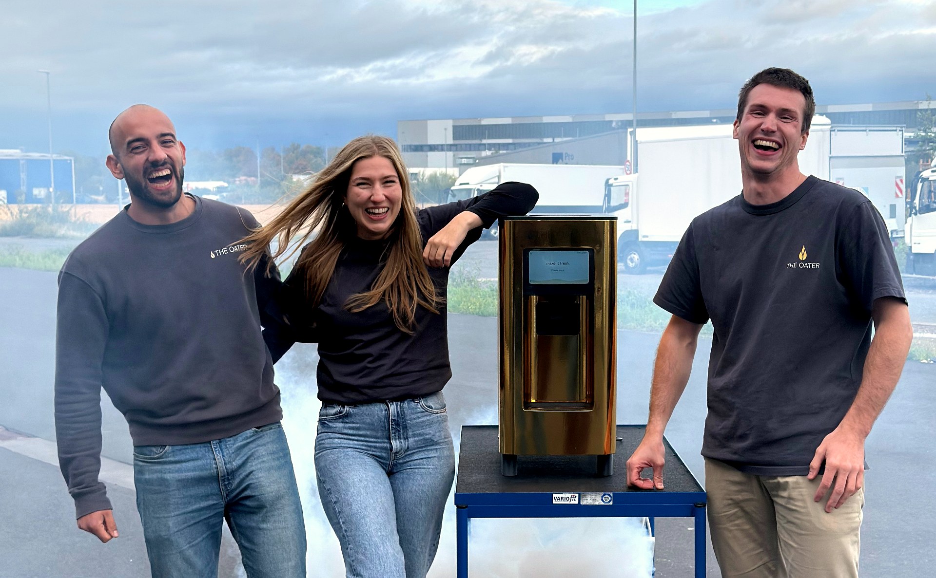 Drei Teammitglieder lachen herzhaft um die goldene The Oater Maschine auf einem Tisch