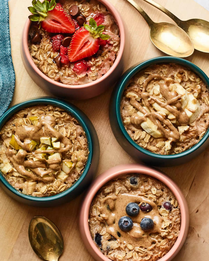 Vier Schälchen Baked Oats mit Erdnussmus, Erdbeeren, Banane und Blaubeeren